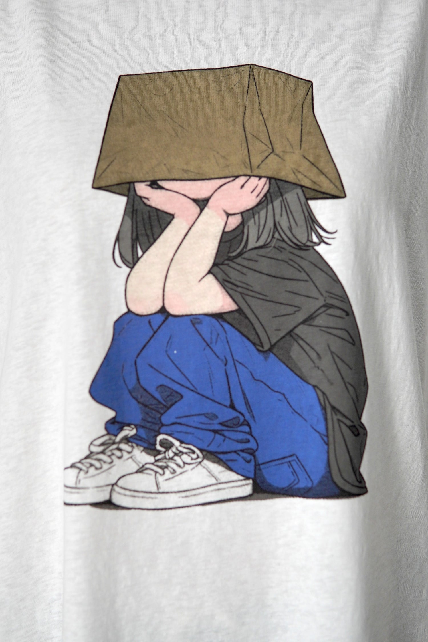 Detaliu al imprimeului de pe tricoul alb, reprezentând o fată desenată cu pantaloni albaștri și cutie pe cap.