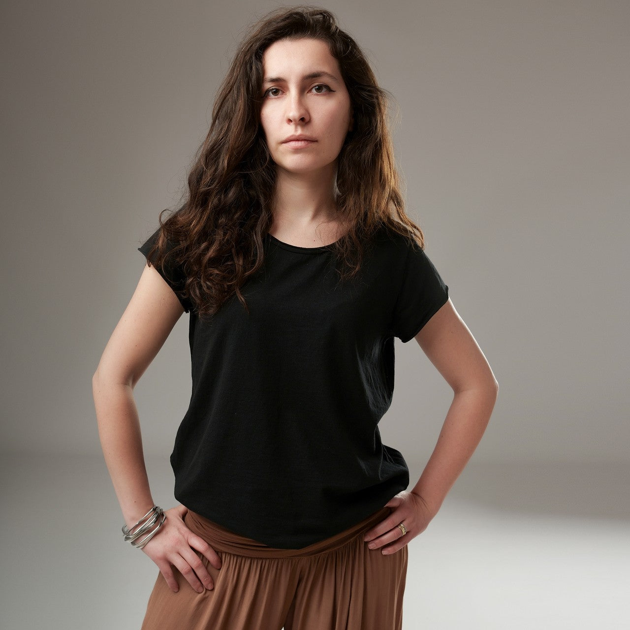  Tricou basic negru cu mâneci scurte și croială ușor evazată, purtat de model cu pantaloni vaporoși.