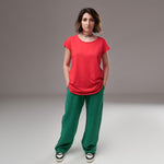 Tricou roz din bumbac cu croială lejeră și mâneci scurte, purtat de model cu pantaloni verzi.