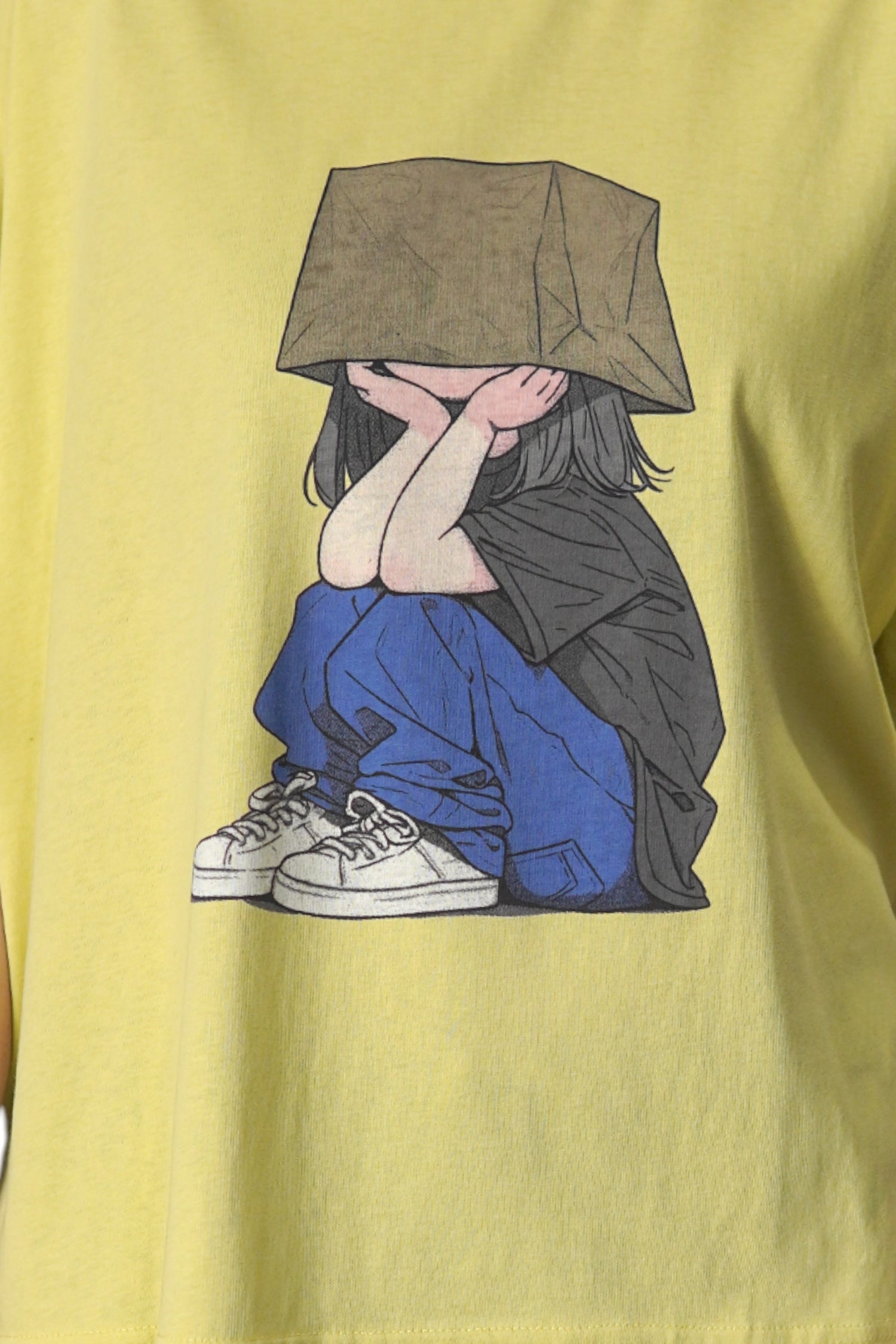 Prim-plan pe imprimeul colorat al tricoului galben oversized, cu o fată în pantaloni albaștri.