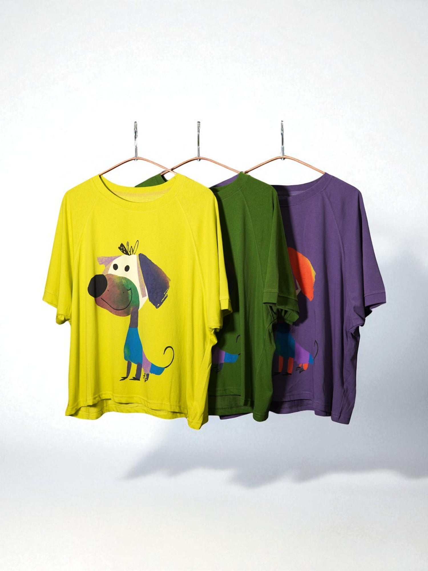 Tricouri oversize galben, verde și violet cu imprimeu colorat cu cățel simpatic, agățate pe umerașe