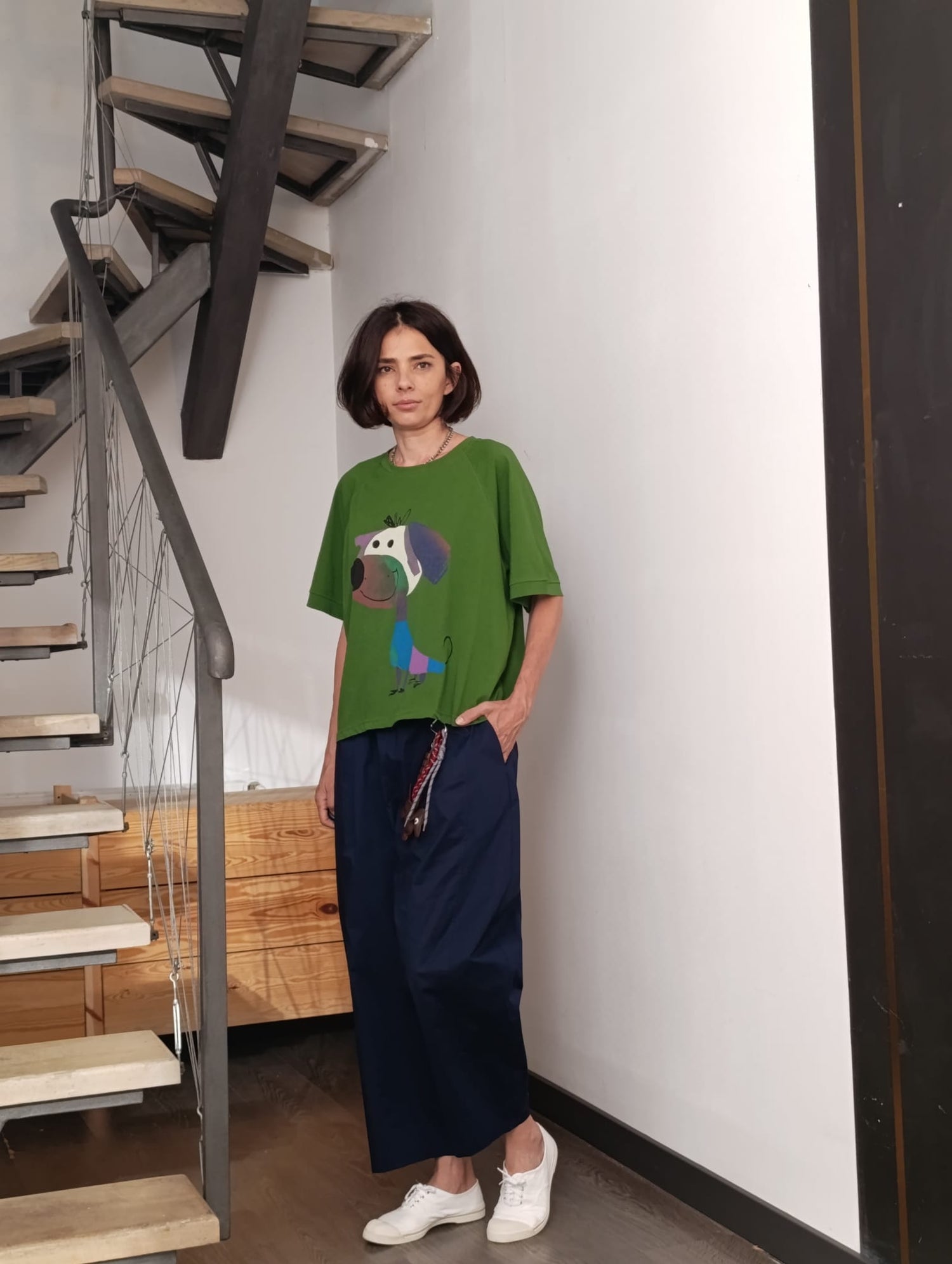 Tricou verde cu imprimeu haios, purtat cu pantaloni bleumarin și pantofi sport