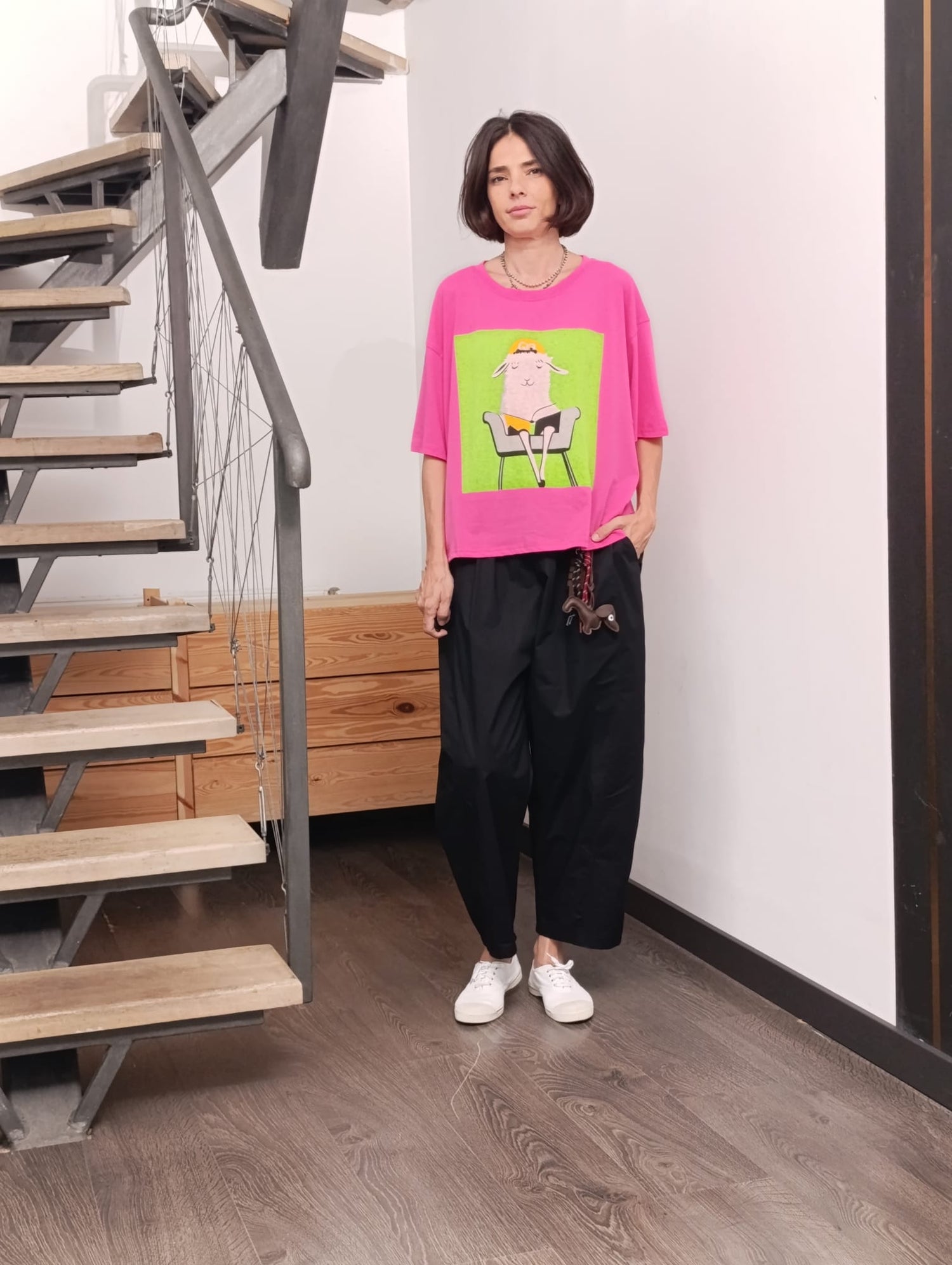  Femeie purtând tricou roz cu lămă imprimată și pantaloni negri, fundal interior