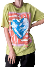 Tricou verde pictat cu inimă albastră, purtat lejer pe o parte
