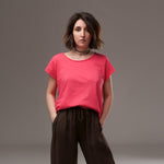 Tricou simplu din bumbac roz intens, cu guler rotund și mâneci scurte, purtat într-o ținută casual cu pantaloni maro largi.