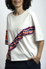 Tricou alb cu volane rainbow aplicate diagonal, croială lejeră și mânecă scurtă.