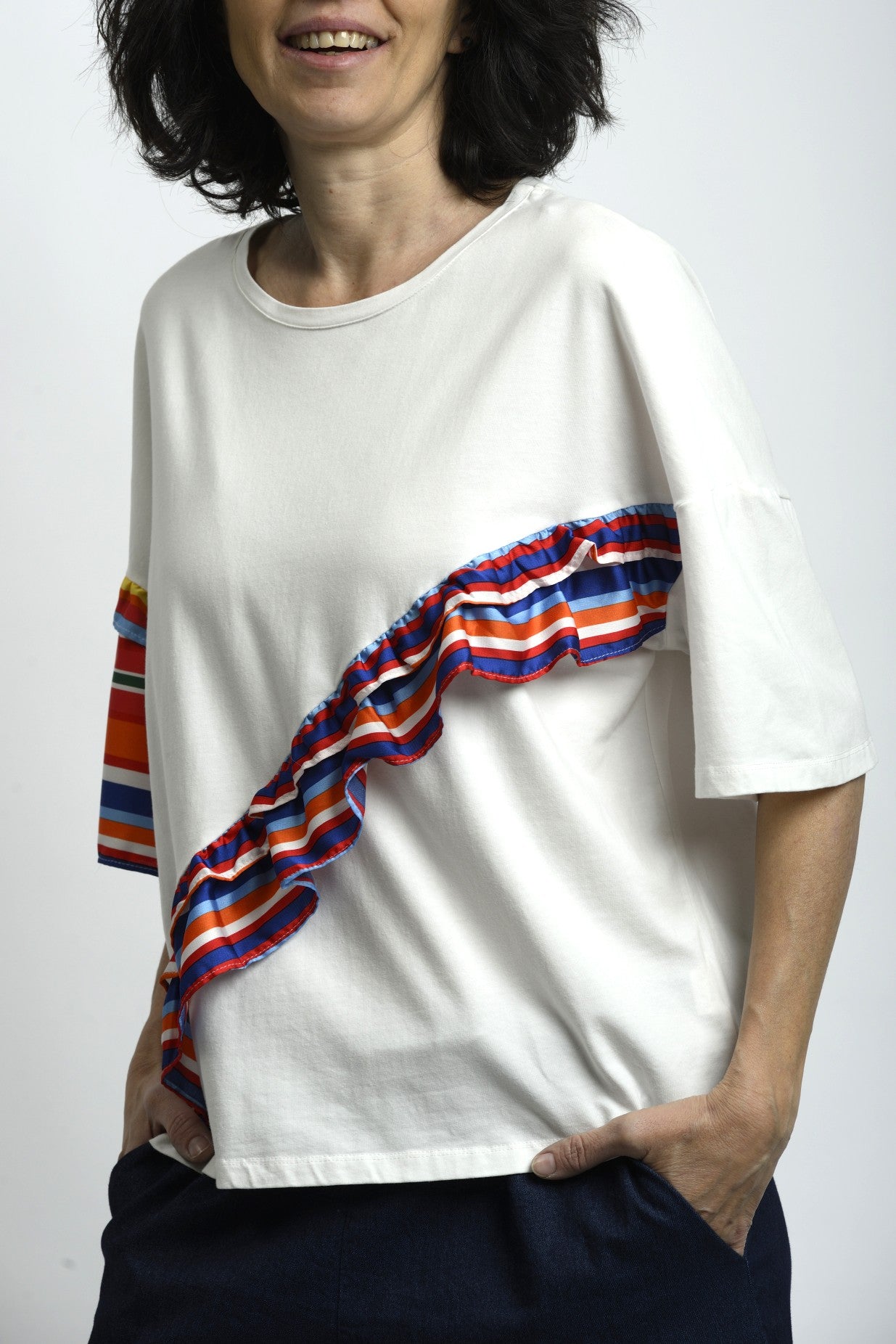 Tricou alb cu volane rainbow aplicate diagonal, croială lejeră și mânecă scurtă.