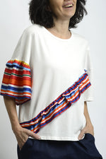 Vedere laterală a tricoului cu volane multicolore și umeri căzuți.