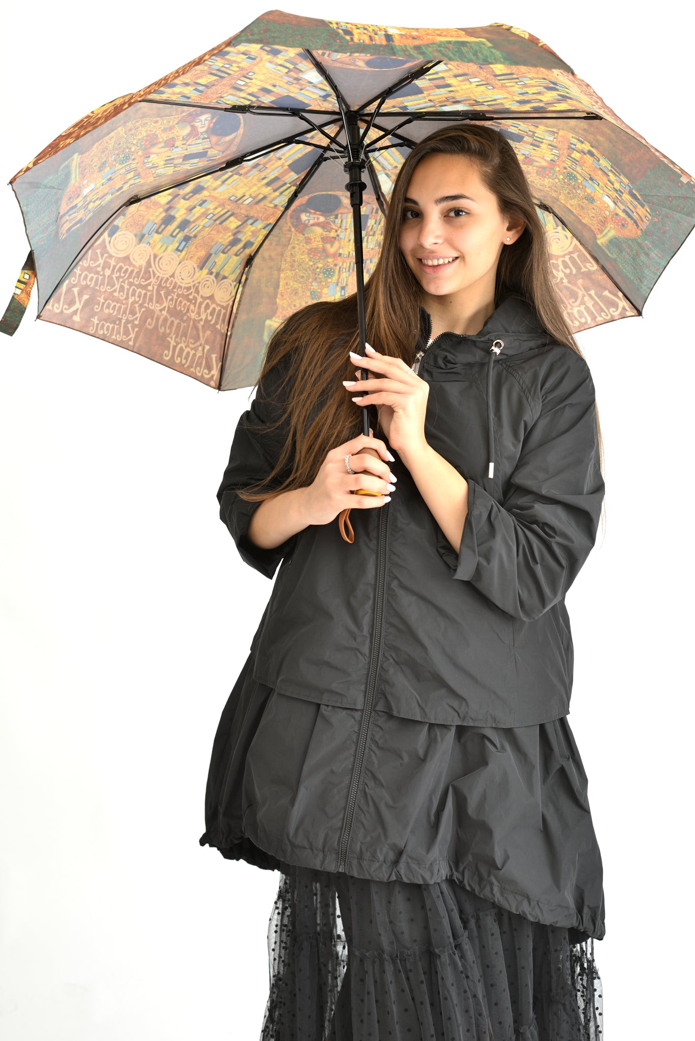 Femeie ținând o umbrelă cu design inspirat din pictura lui Gustav Klimt, pe fundal neutru.