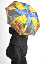 Umbrelă deschisă cu imprimeu inspirat din pictura „Café Terrace at Night” a lui Vincent van Gogh, în nuanțe de albastru și galben intens.