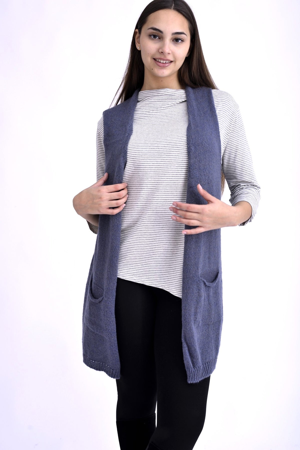 Model purtând o vestă lungă tricotată bleumarin cu buzunare și croială deschisă, completată de o bluză cu dungi și colanți negri.
