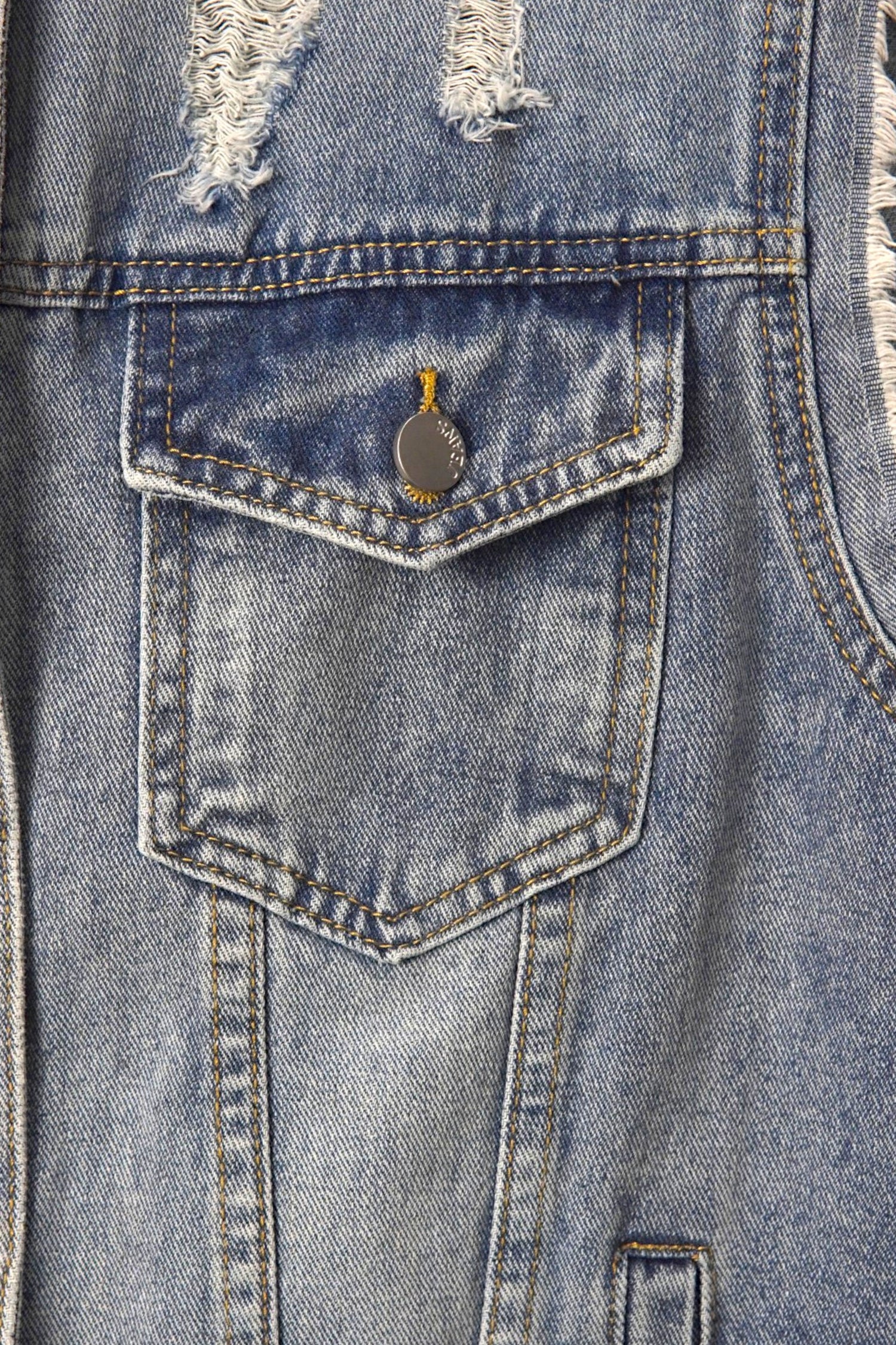 Buzunar frontal cu clapetă și nasture metalic al unei veste din denim albastru, cu cusături contrastante.