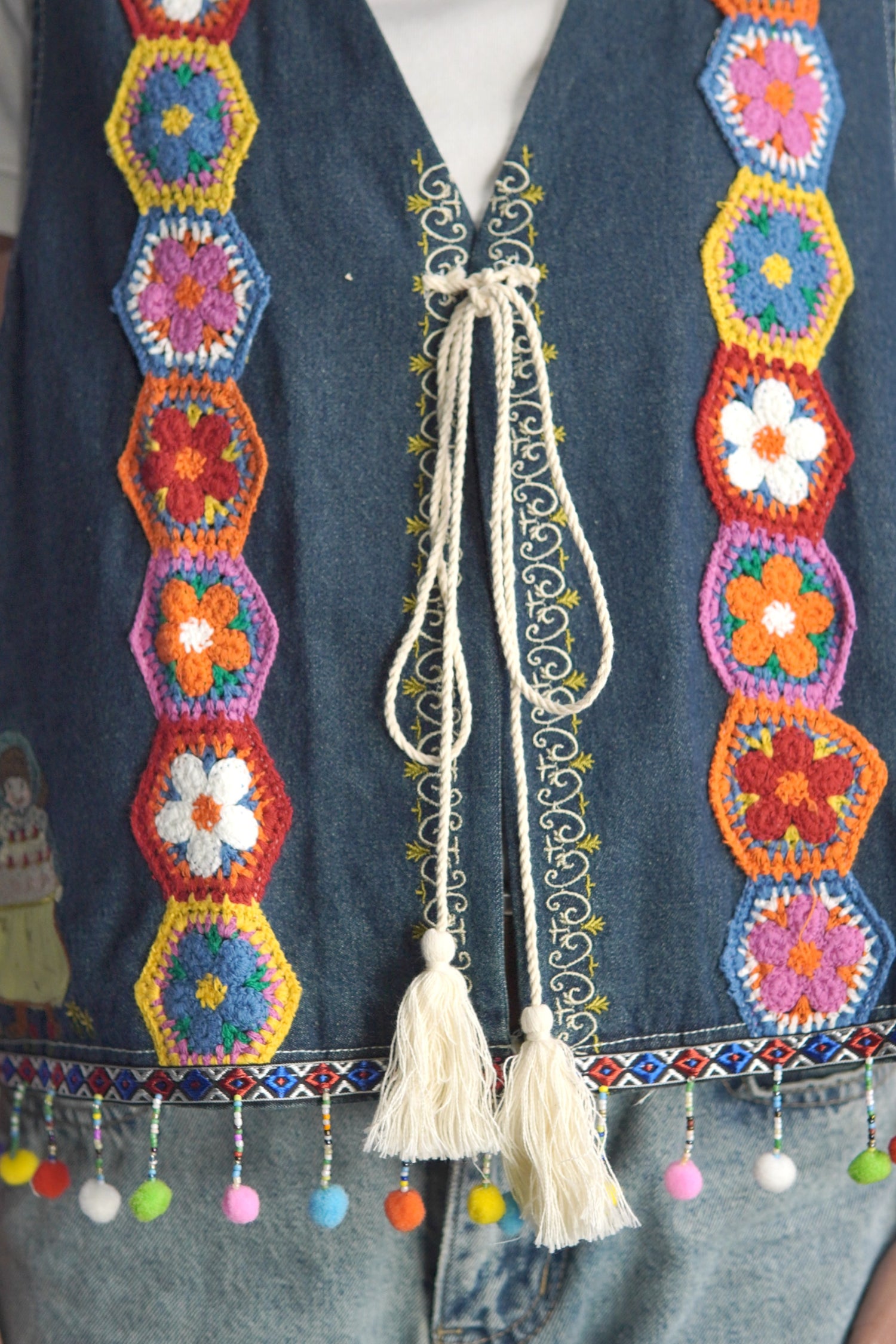 Prim-plan pe șnurul decorativ și cusăturile florale ale vestei boho din bumbac.