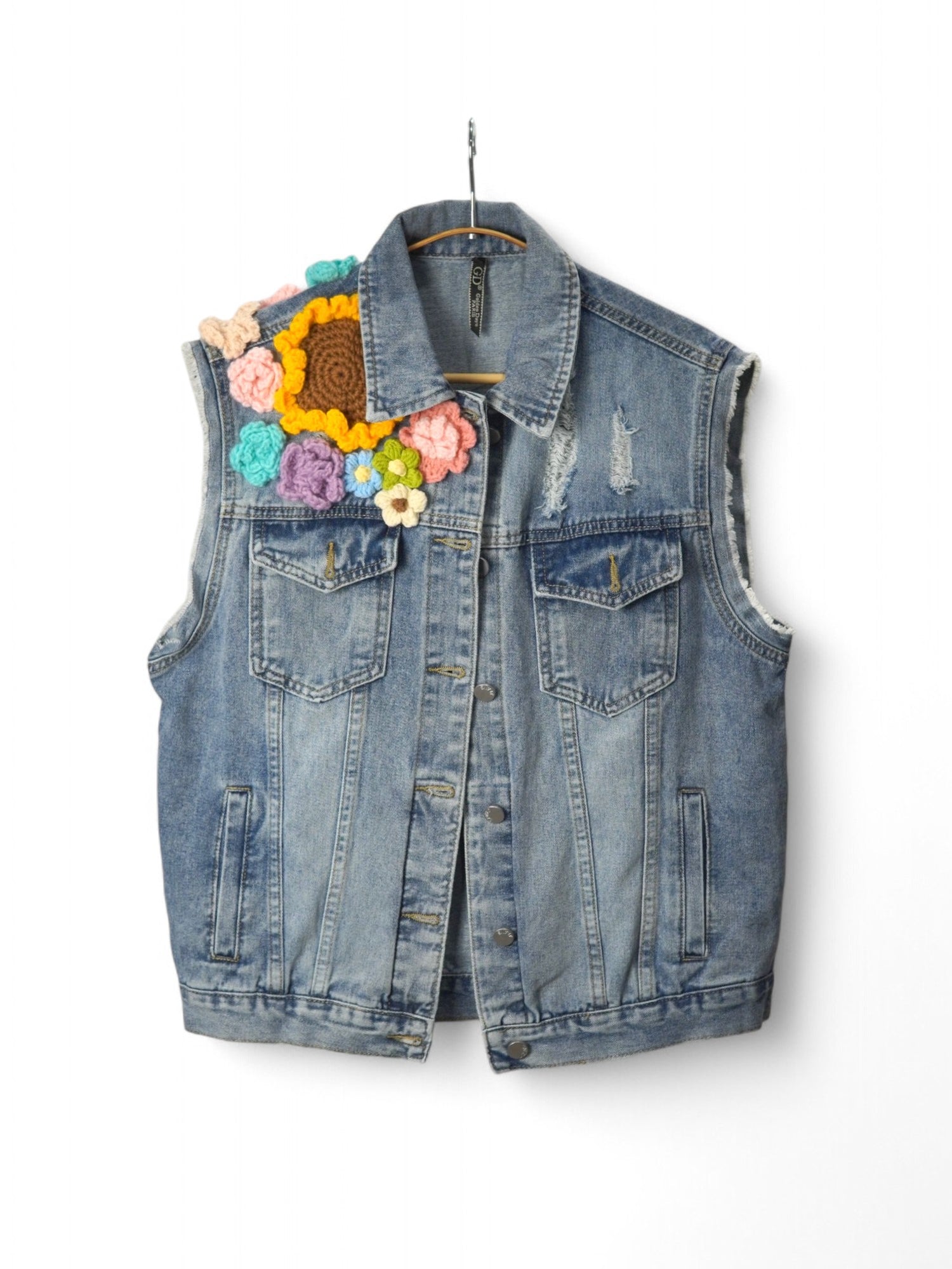 Vesta din denim cu buzunare frontale, nasturi metalici și aplicații florale croșetate colorate.