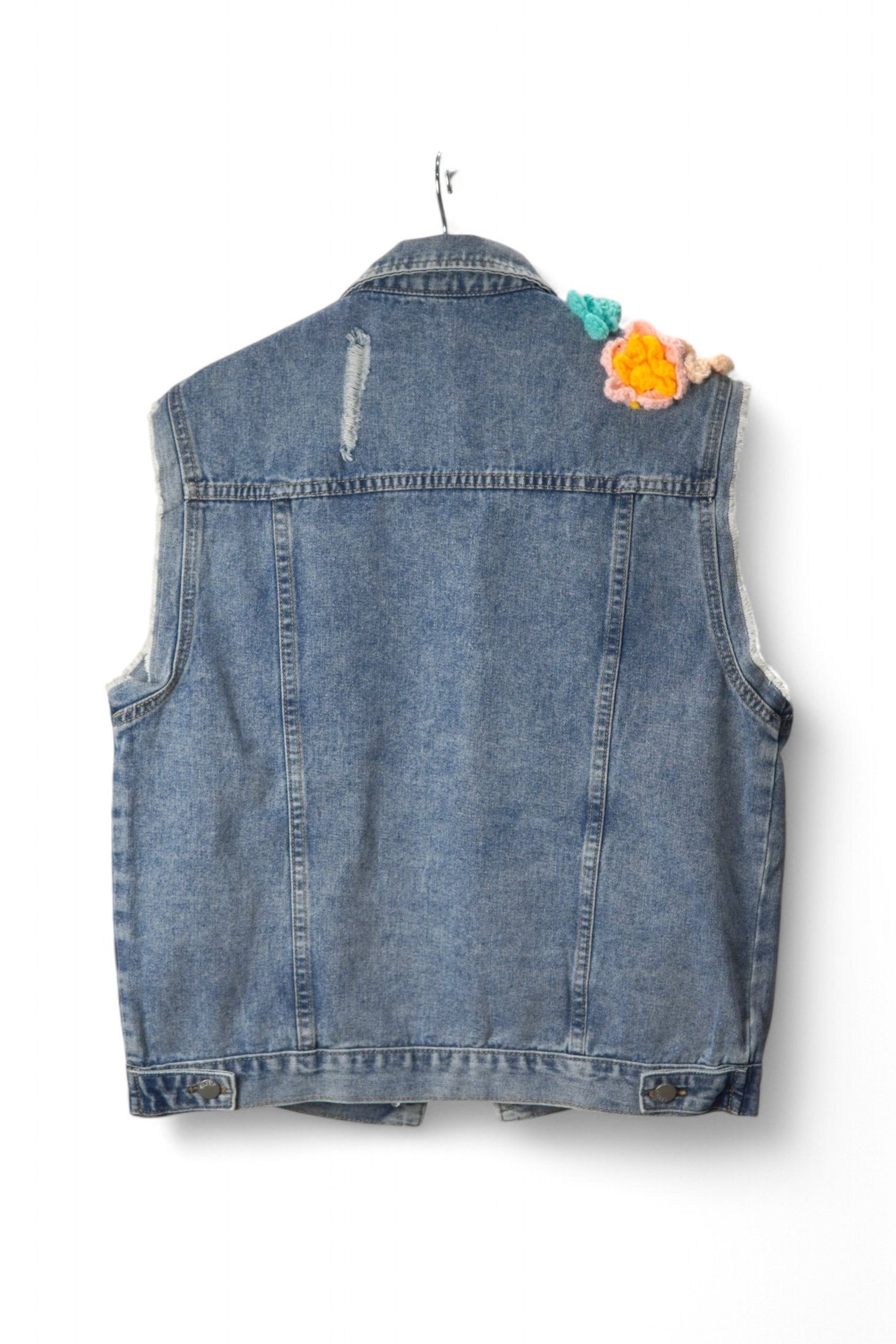 Spatele unei veste din denim cu detalii ușor uzate și o aplicație croșetată în colțul umărului.