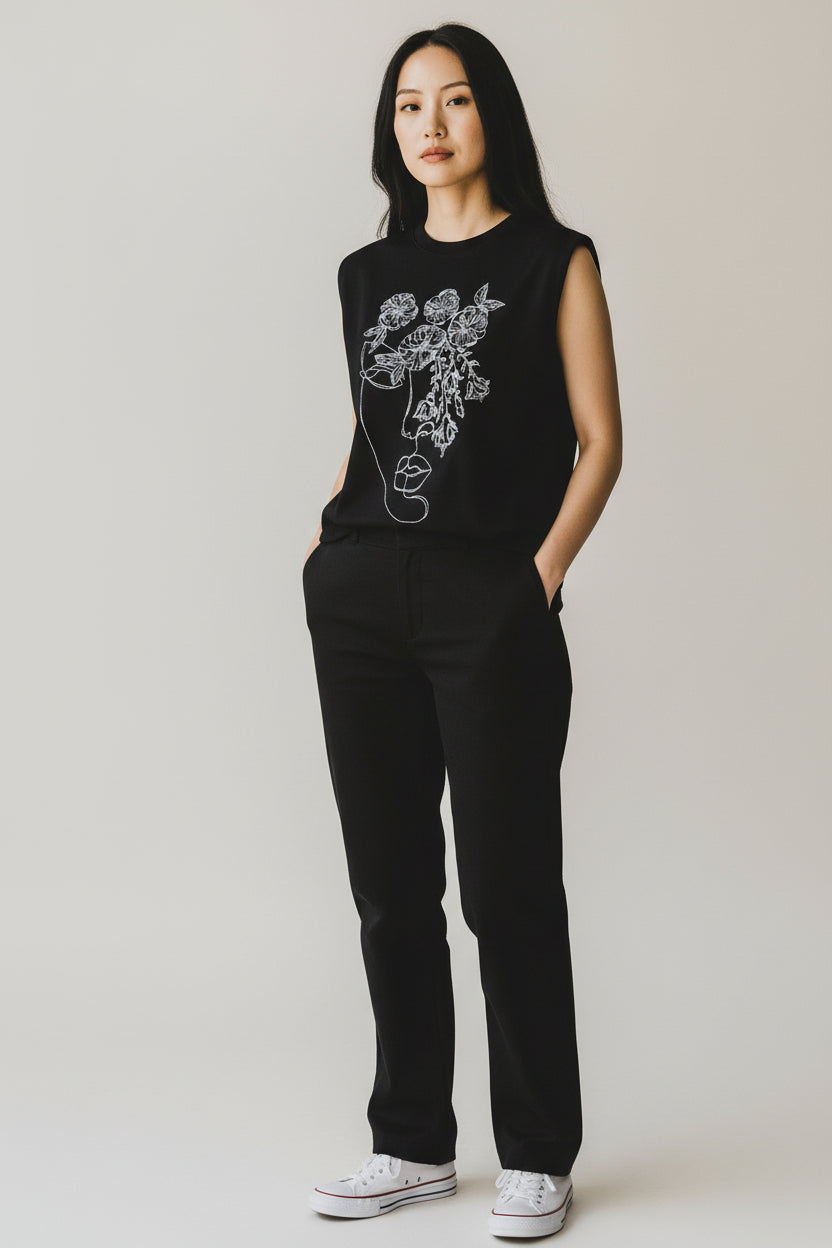 Vestă neagră cu broderie, purtată într-o ținută minimalistă, cu pantaloni negri și adidași albi.