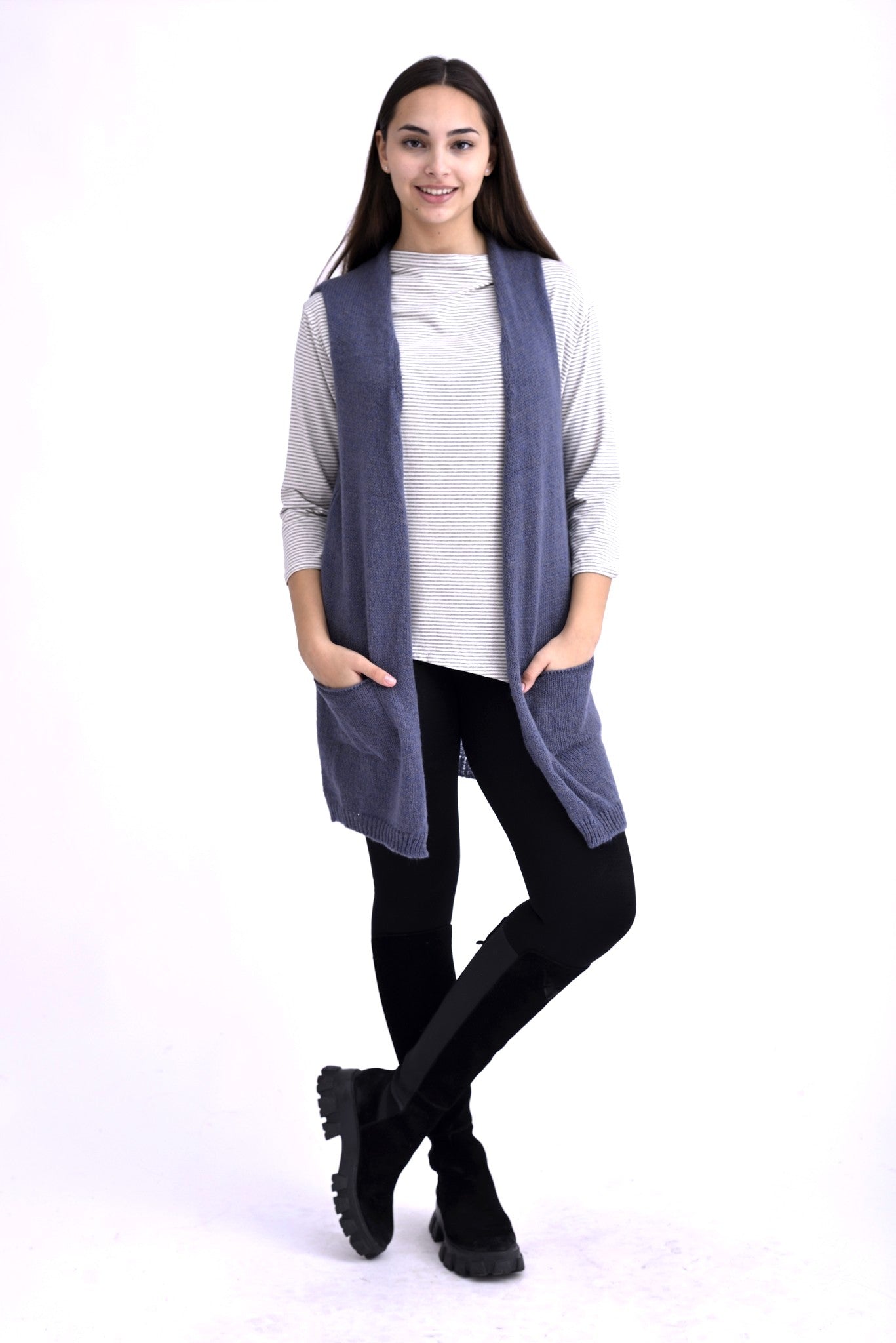 Model purtând o vestă tricotată bleumarin, fără mâneci, cu buzunare frontale și croială lejeră, peste o bluză în dungi alb-gri.