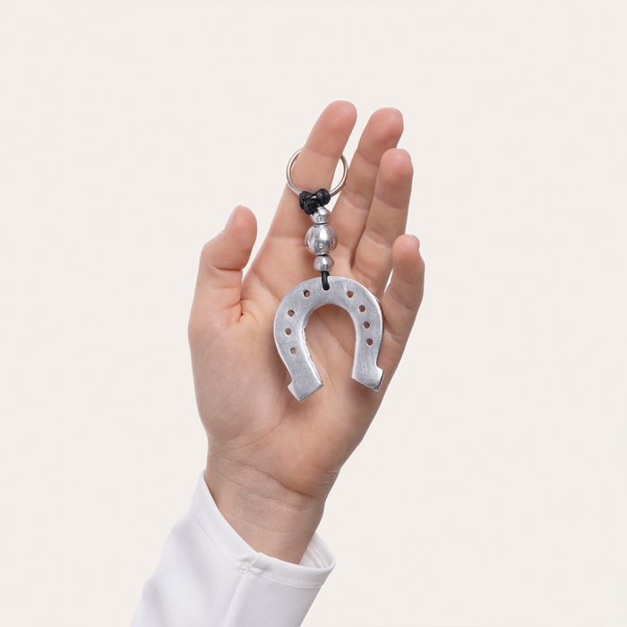 Breloc handmade din aluminiu reciclat, în formă de potcoavă, ținut în mână – simbol al norocului și design eco-friendly.