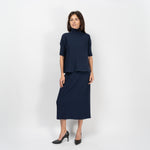 Femeie purtând pulover bleumarin cu mânecă scurtă și fustă plisată, într-un look casual-elegant