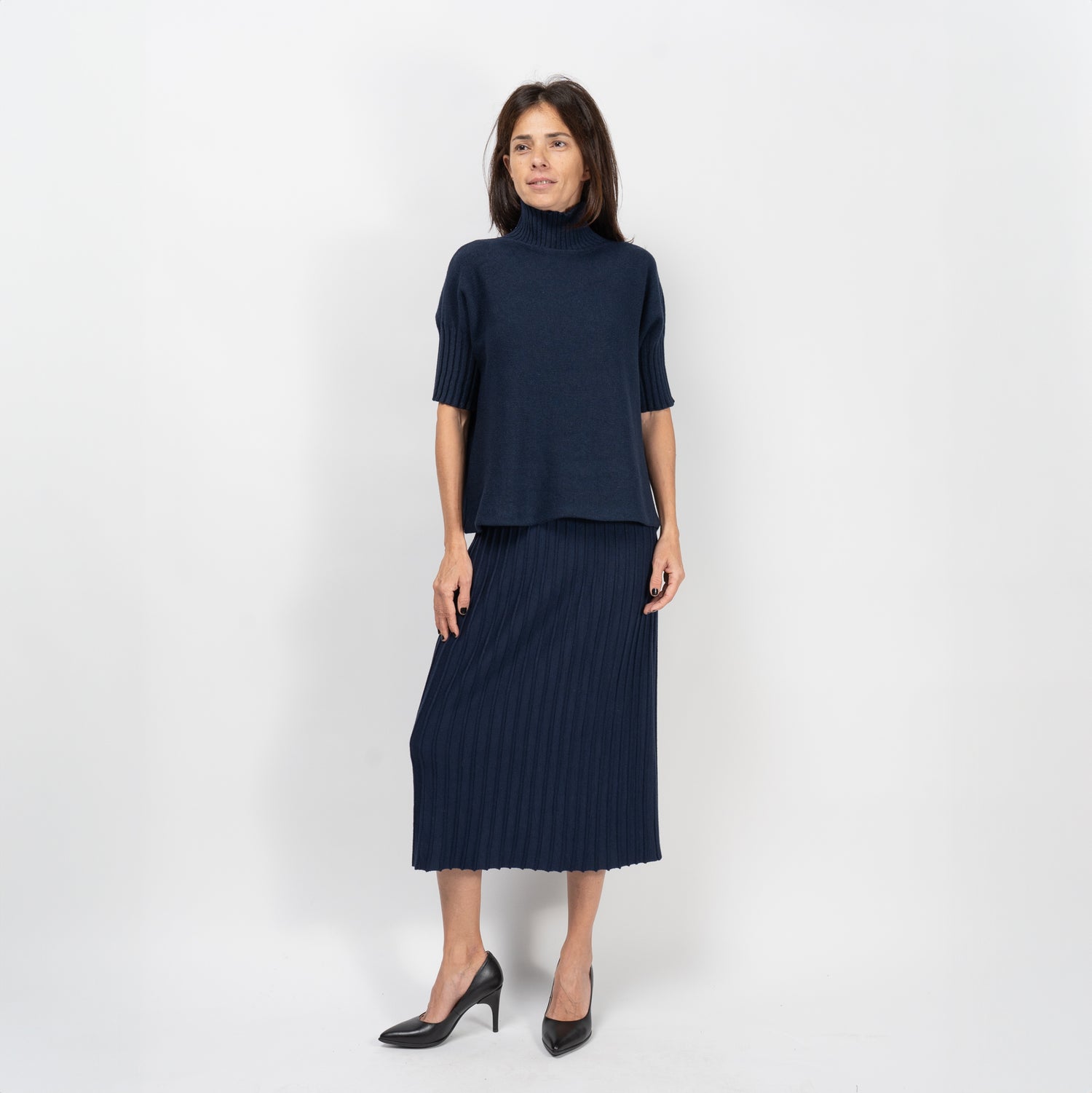 Femeie purtând pulover bleumarin cu mânecă scurtă și fustă plisată, într-un look casual-elegant