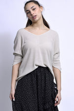 All Above Boutique beige knit V-neck sweater with dropped shoulders and relaxed fit, paired with a black polka dot skirt.