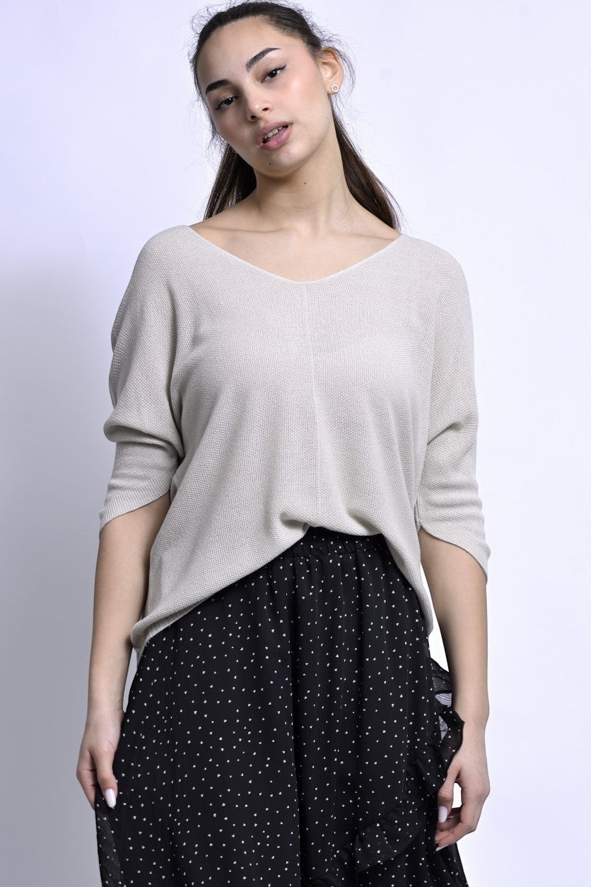 All Above Boutique beige knit V-neck sweater with dropped shoulders and relaxed fit, paired with a black polka dot skirt.