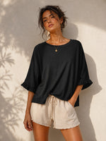 All Above Boutique black cotton 3/4 sleeve relaxed fit blouse with ruffled cuffs, paired with beige linen shorts.