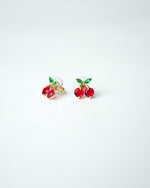 All Above Boutique small gold cherry stud earrings with red gems and green leaves.
