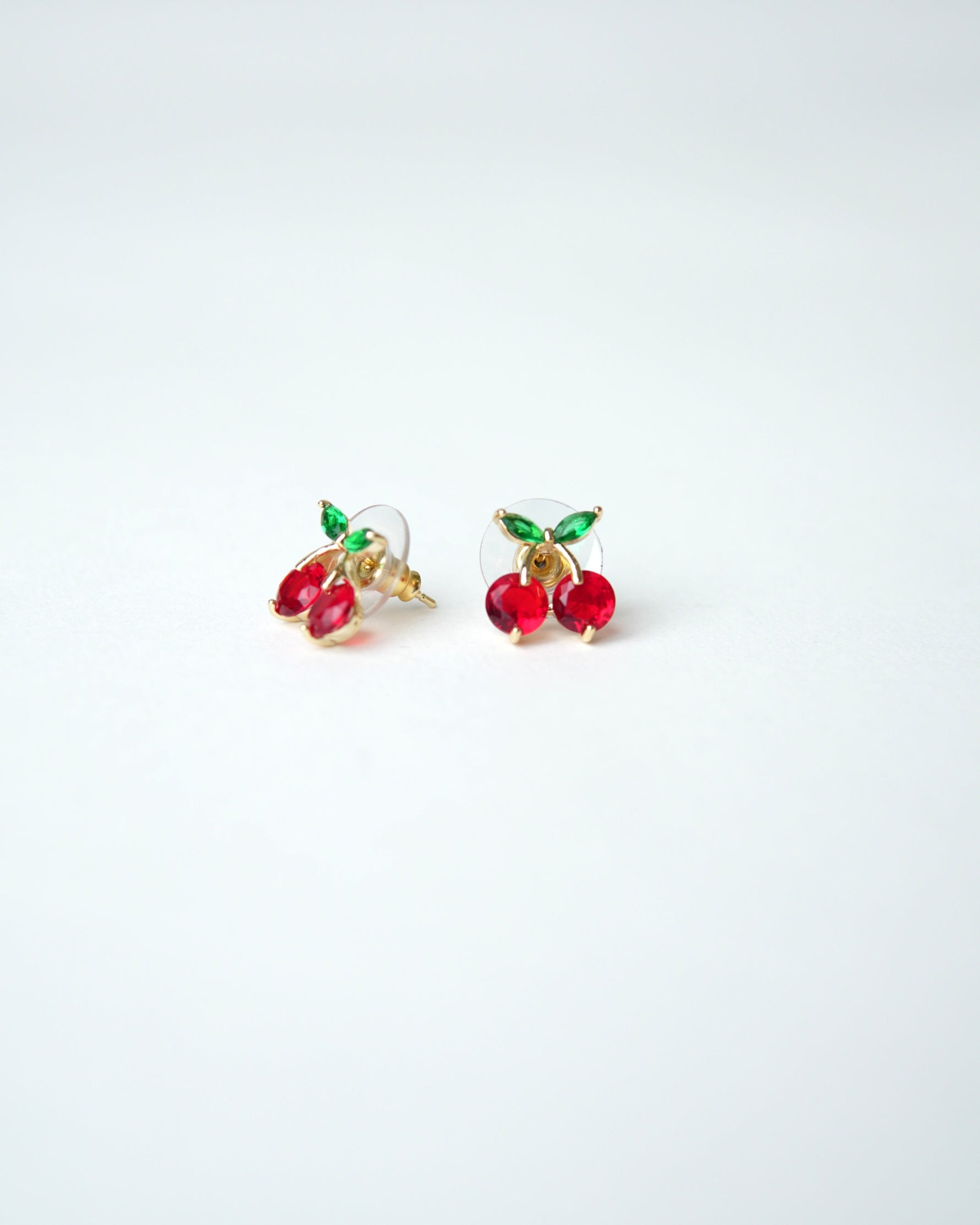 All Above Boutique small gold cherry stud earrings with red gems and green leaves.