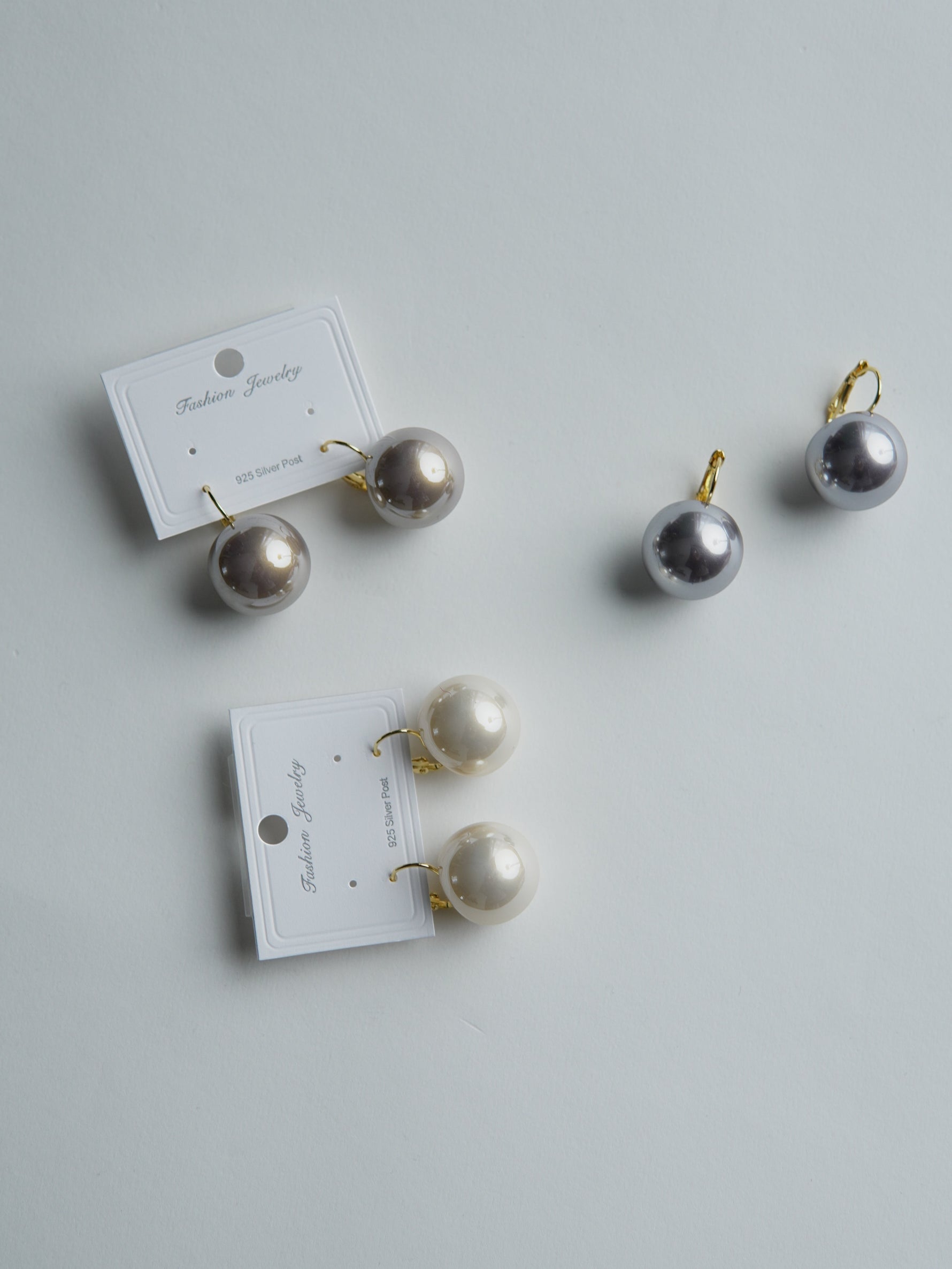 All Above Boutique pearl drop earrings in cream and grey, made with stainless steel and synthetic pearls. Classic design.