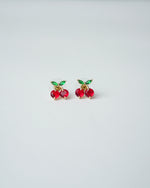 All Above Boutique small red cherry stud earrings with green leaf details, gold tone.