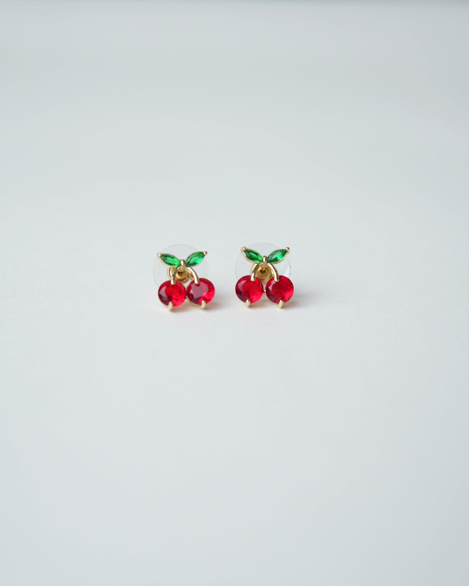 All Above Boutique small red cherry stud earrings with green leaf details, gold tone.