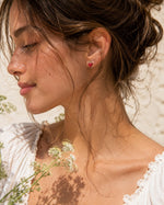 All Above Boutique small red strawberry stud earrings with a glossy finish, worn by a model.