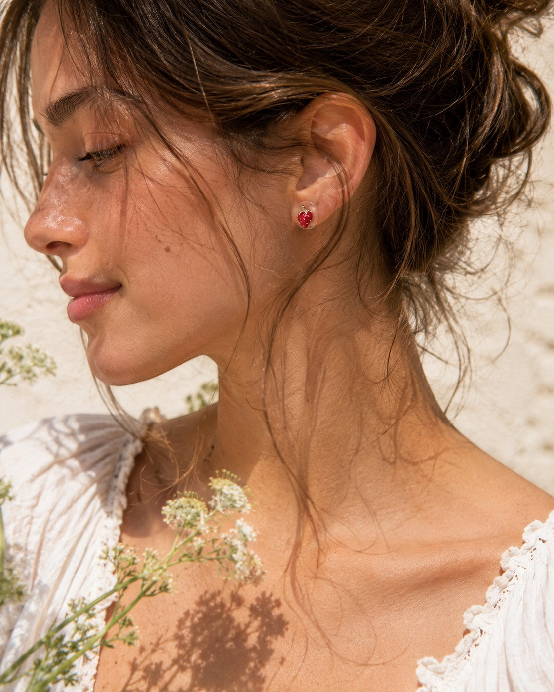 All Above Boutique small red strawberry stud earrings with a glossy finish, worn by a model.