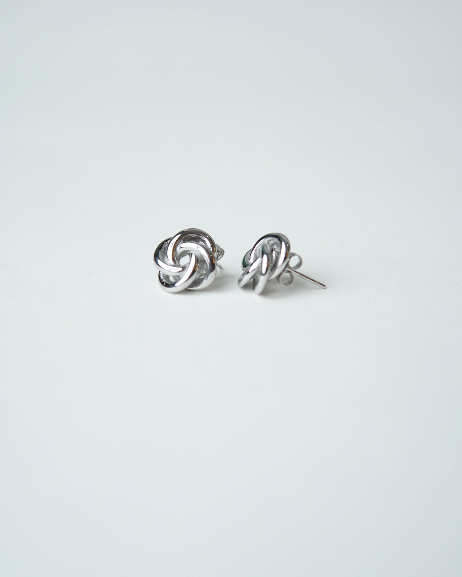 All Above Boutique silver-tone knot stud earrings with a polished finish and floral-inspired design.