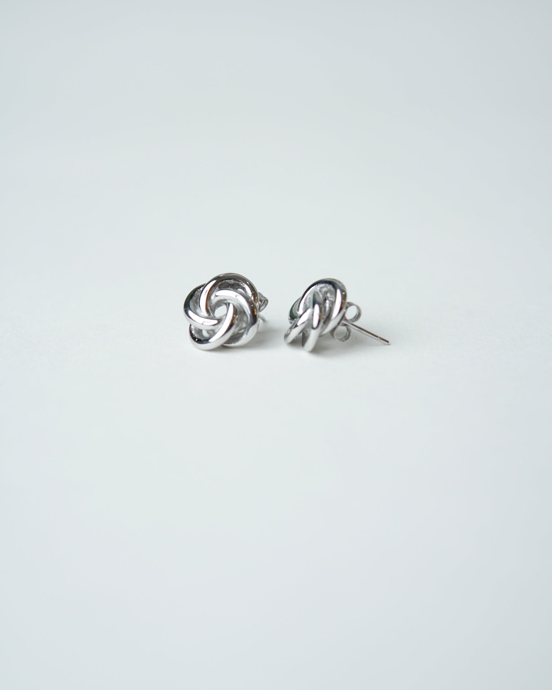All Above Boutique silver-tone knot stud earrings with a polished finish and floral-inspired design.
