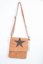 All Above Boutique tan suede crossbody bag with black star detail and adjustable strap.