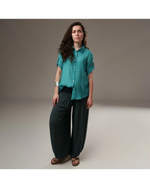 All Above Boutique teal rayon short-sleeve button-up shirt with cuffed sleeves and asymmetric hem, worn by a model with dark hair.