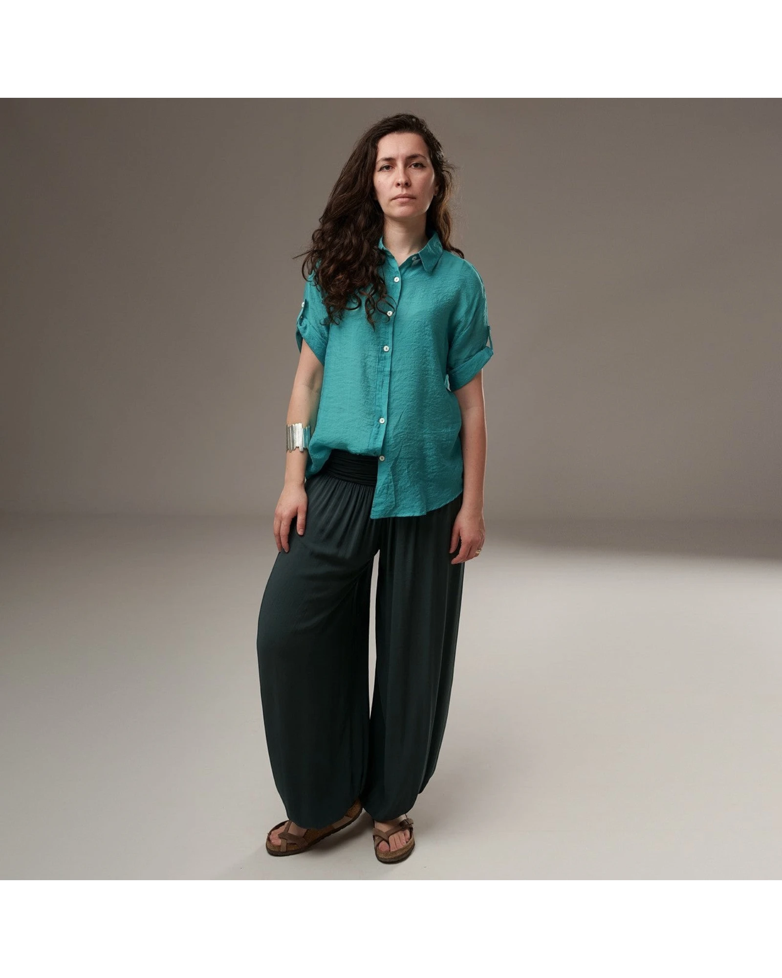 All Above Boutique teal rayon short-sleeve button-up shirt with cuffed sleeves and asymmetric hem, worn by a model with dark hair.