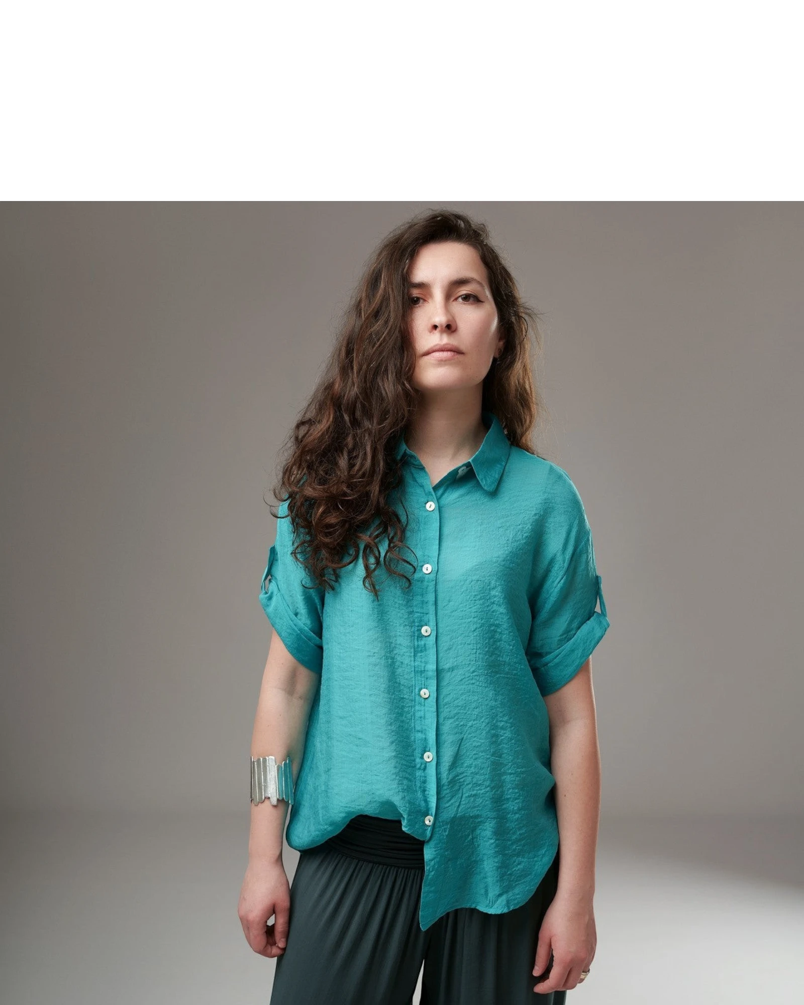 All Above Boutique teal rayon relaxed fit short sleeve button-up shirt with asymmetric hem and rolled cuffs.