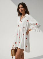 All Above Boutique white oversized shirt dress with strawberry print and 3/4 ruffled sleeves. Model is holding a straw bag.