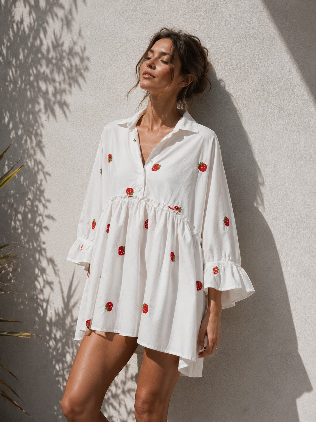 All Above Boutique white oversized shirt dress with 3/4 sleeves and a playful strawberry print, featuring ruffled cuffs and a tiered hem.