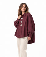 Cămașă oversize din bumbac roșu închis, cu nasturi mari tip oglindă și tiv mai lung la spate, purtată pe model, vedere laterală - All Above Boutique
