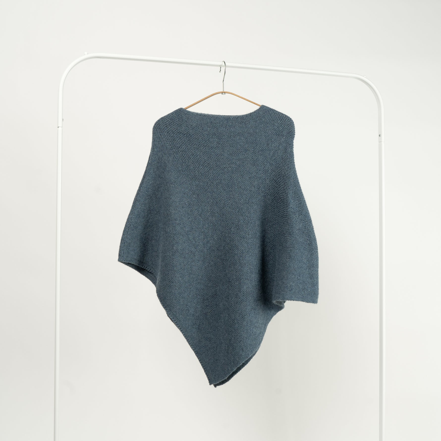 Capă tricotată cu 30% lână, de culoare bleu, cu croială asimetrică.