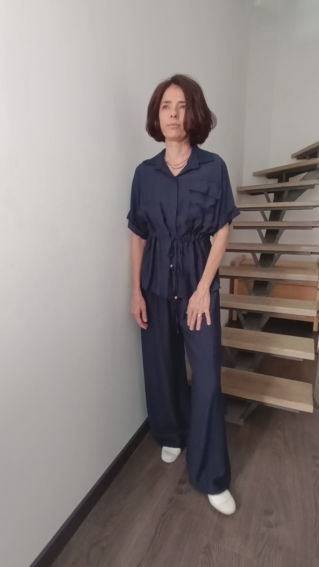 Compleu satinat bleumarin cu bluză cu cordon în talie și pantaloni largi, purtat de model în fața unei scări interioare