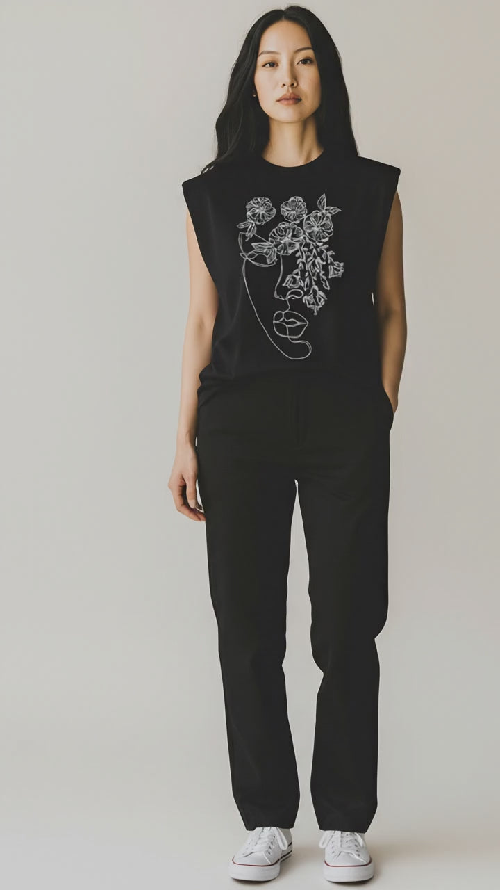 Vestă neagră cu broderie, purtată într-o ținută minimalistă, cu pantaloni negri și adidași albi.