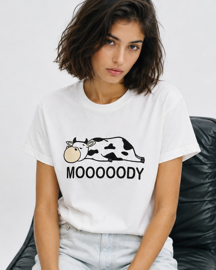 Femeie purtând tricou alb cu imprimeu văcuță și mesaj Moooody